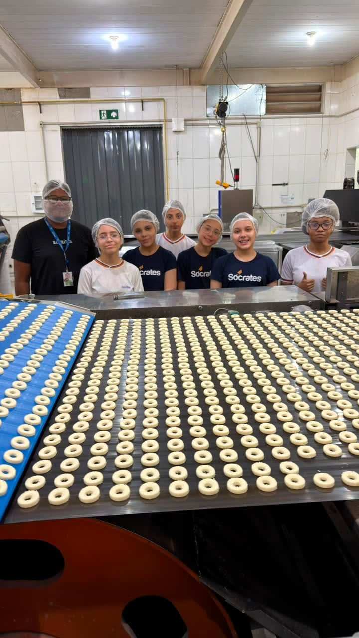 Alunos de touca observando a esteira com centenas de biscoitos ainda crus