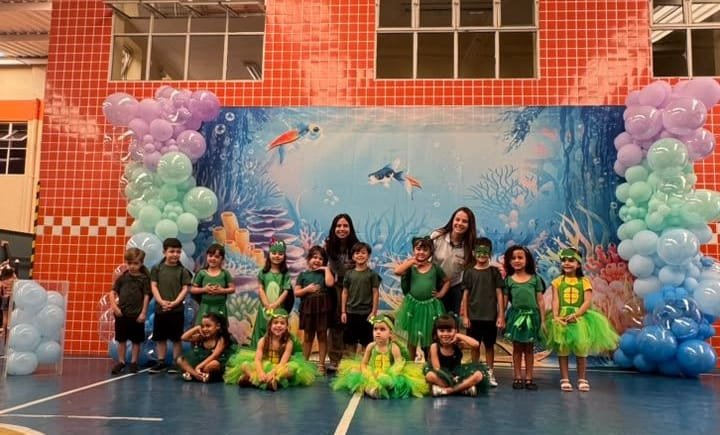 Turma da Educação Infantil fantasiada de verde em frente ao cenário de fundo do mar