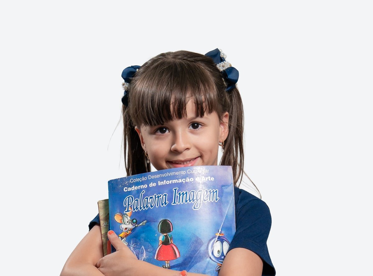 Criança da Educação Infantil do Colégio Sócrates abraçando seus livros e sorrindo