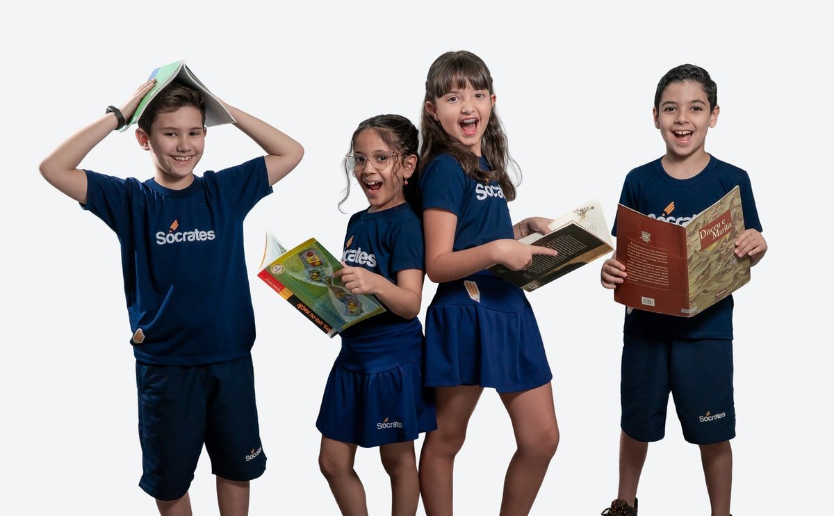 Quatro alunos do Colégio Sócrates sorrindo com seus livros nas mãos